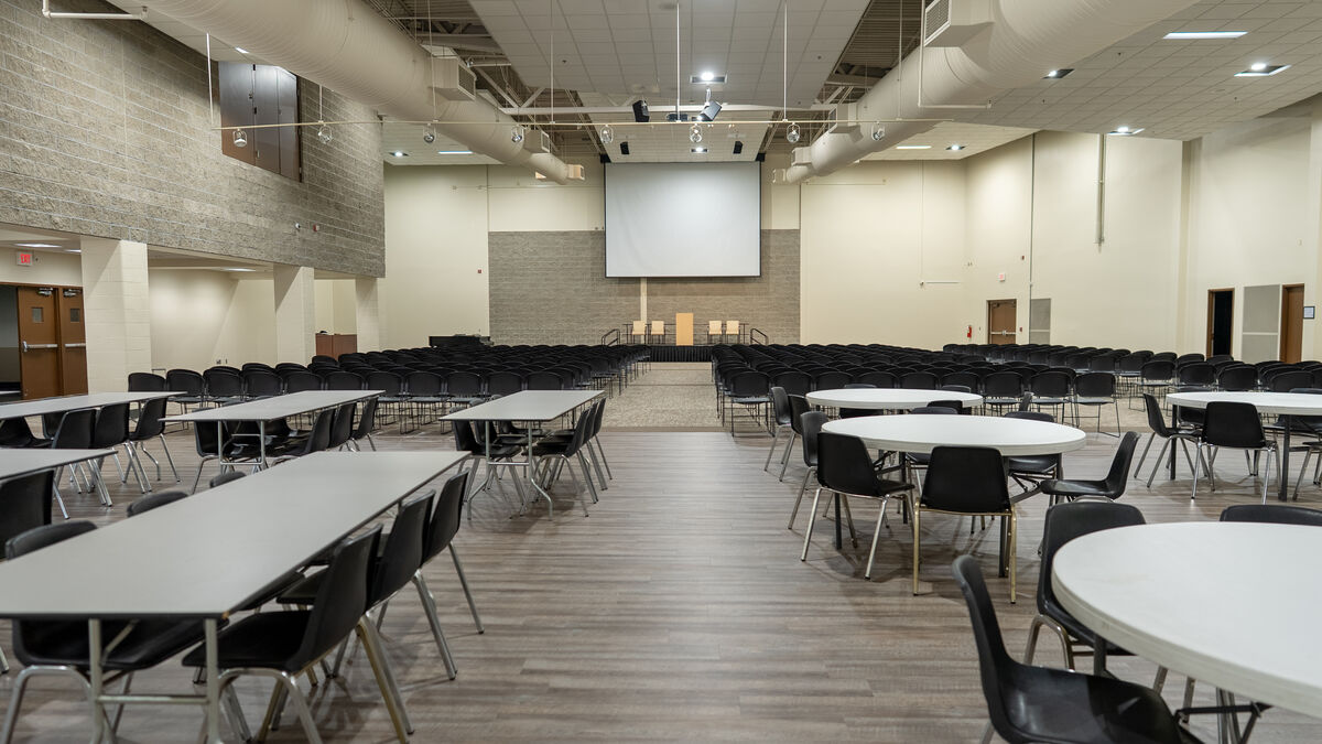 The Cornerstone Auditorium set for an event — long and round tables, rows of chairs, and a stage with a projection screen